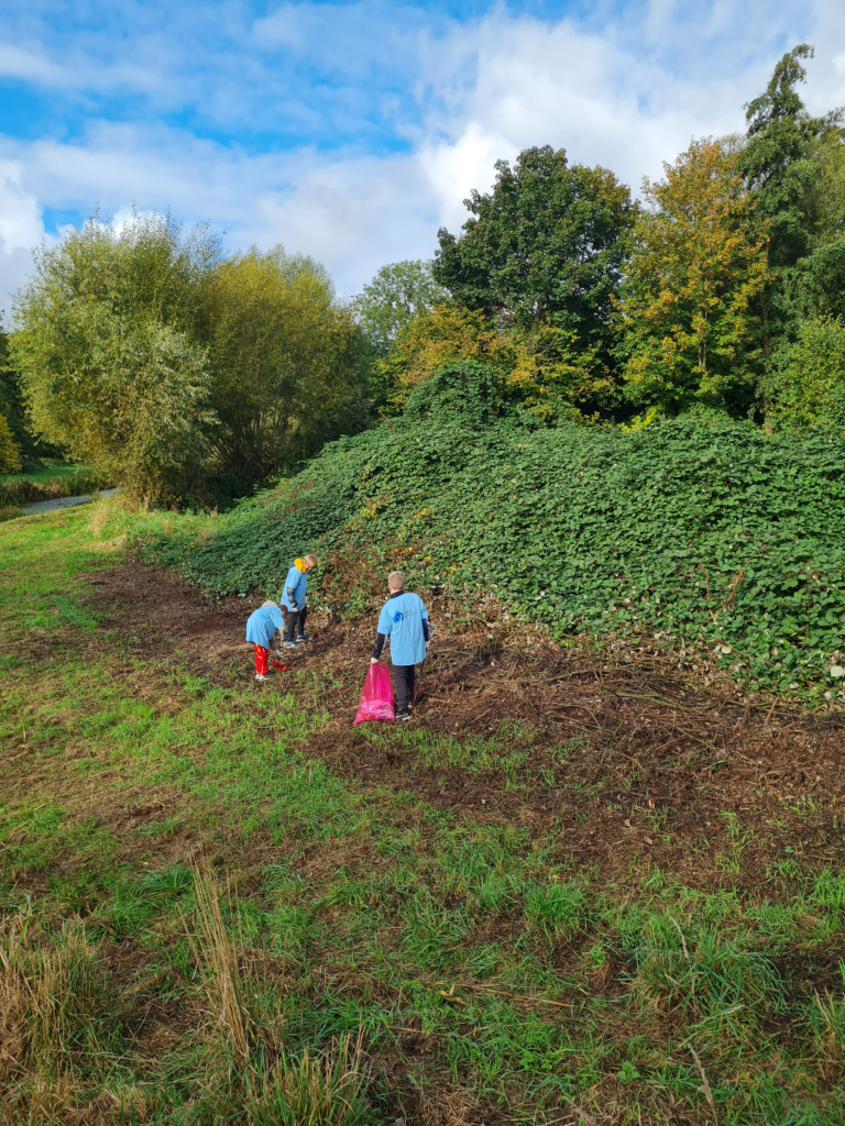 Drei Kinder in farbenfroher Kleidung gehen einen grasbewachsenen Hügel hinauf, der mit dichtem grünen Laub bedeckt ist, mit Bäumen und einem teilweise bewölkten blauen Himmel im Hintergrund. Die Szene ist friedlich und im Freien.